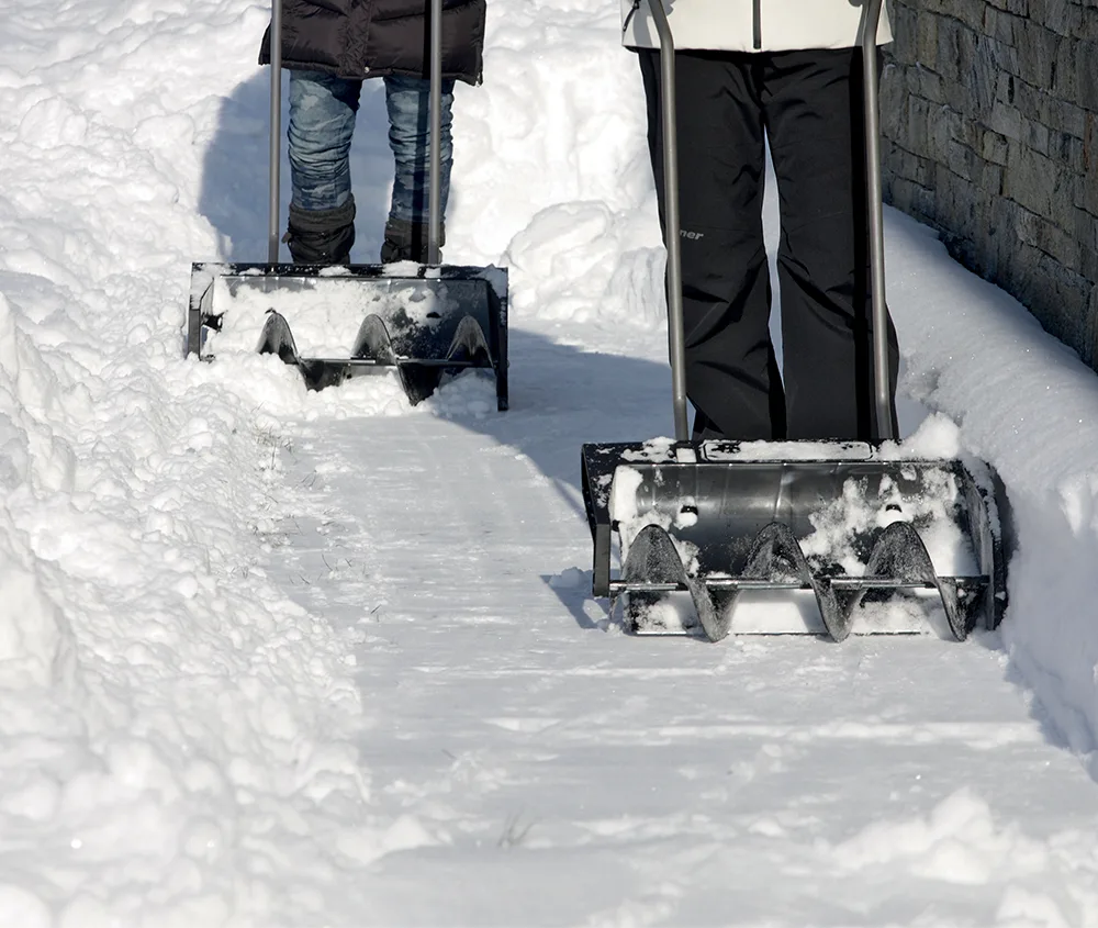 To personer måker nysnø fra en gårdsplass med Snow Mover